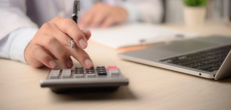 Doctor at desk typing on a calculator.