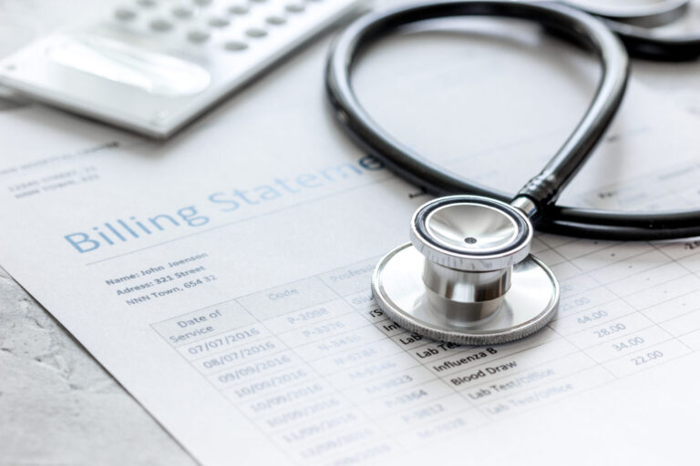 A stethoscope rests on top of a medical billing statement with a calculator resting nearby.